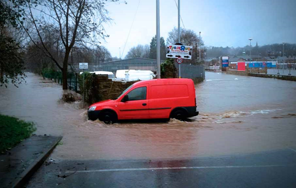 Red van driving through murky flood waters outside of Tesco Car Park